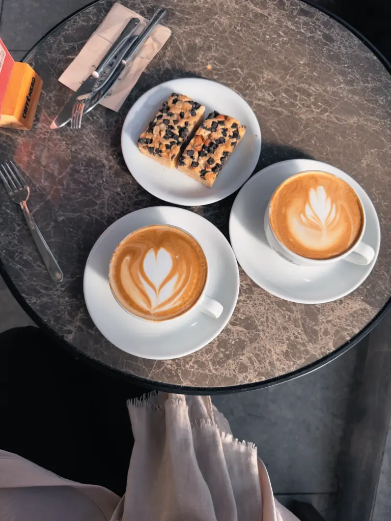 Zwei Kaffeetassen und ein Kuchen auf einem Café-Tisch – Symbol für offene Geldgespräche in gemütlicher Atmosphäre.